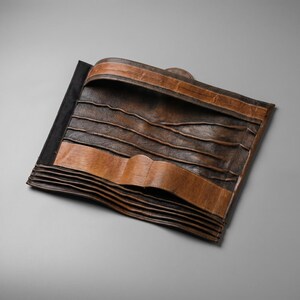 May include: A brown leather tool roll featuring multiple horizontal pockets for storage. The organizer has a dark brown textured finish with lighter tan leather accents along the top and bottom edges, designed to fold and secure various small items.