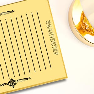 Könnte beinhalten: Ein gelber Notizblock mit dem Wort "BRAINDUMP" vertikal in Schwarz gedruckt. Der Notizblock hat schwarze Linien zum Schreiben und dekorative schwarze Verzierungen. Im Hintergrund ist teilweise ein goldfarbenes Objekt zu sehen.