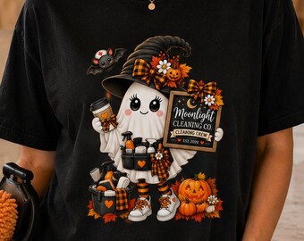 May include: A black t-shirt featuring a graphic of a cartoon ghost wearing a witch hat and holding a cleaning caddy. The ghost is surrounded by pumpkins and autumn leaves. The text on the sign reads Moonlight Cleaning Co. Est 2024.
