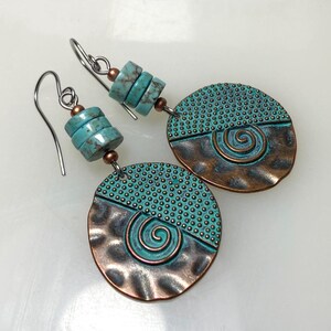 May include: A pair of dangle earrings featuring round, hammered copper-toned discs with a teal patina finish, a spiral design, and a dotted texture. Each earring is accented with three cylindrical turquoise-colored beads and silver-toned hooks.