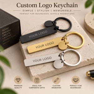May include: Three rectangular metal keychains in black, gold, and silver finishes, each featuring a split ring, a small circular charm, and the engraved text "YOUR LOGO". The keychains are displayed alongside a black box with the text "GOOD BRANDS CREATE LASTING CONNECTIONS" and various icons representing quality, gifts, and engraving.