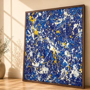 Könnte beinhalten: Ein quadratisches Leinwandgemälde in einem dunkelbraunen Holzrahmen im abstrakt-expressionistischen Stil mit einem tiefblauen Hintergrund, der mit energischen Spritzern und Tropfen aus leuchtend weißer und gelber Farbe überzogen ist.
