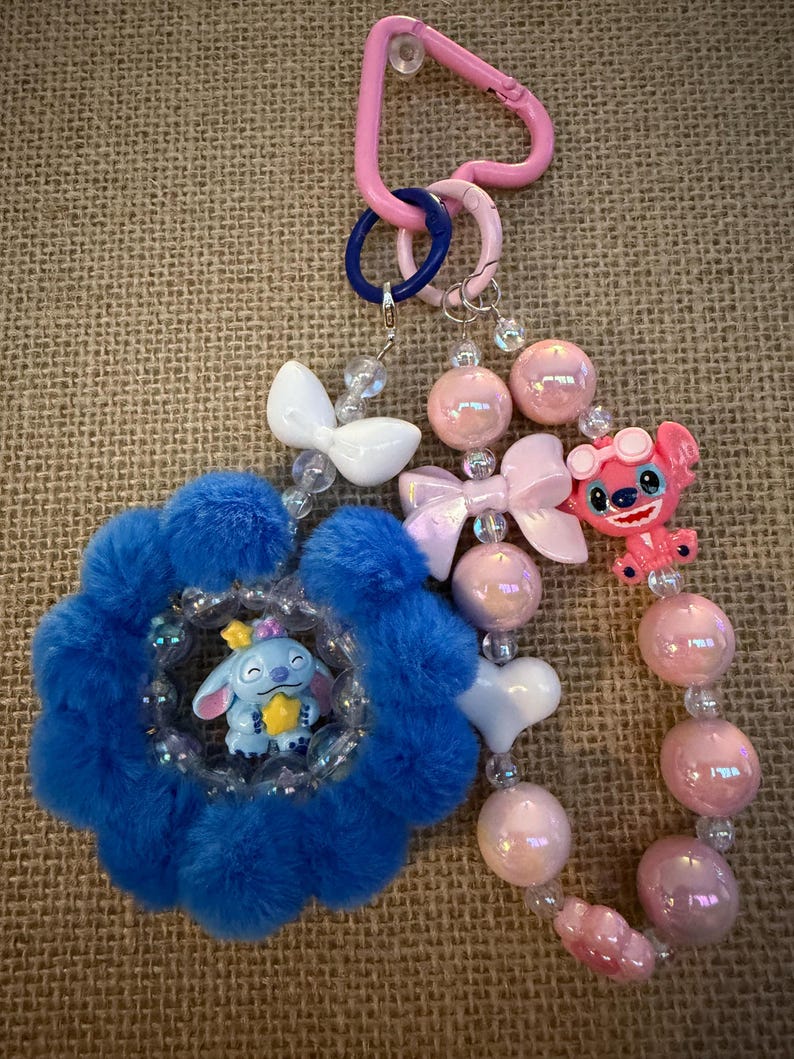 May include: A handmade keychain featuring a blue flower-shaped charm with a Stitch figurine, pink and white beads, and a pink carabiner clip. The keychain includes a pink Stitch figurine with sunglasses.