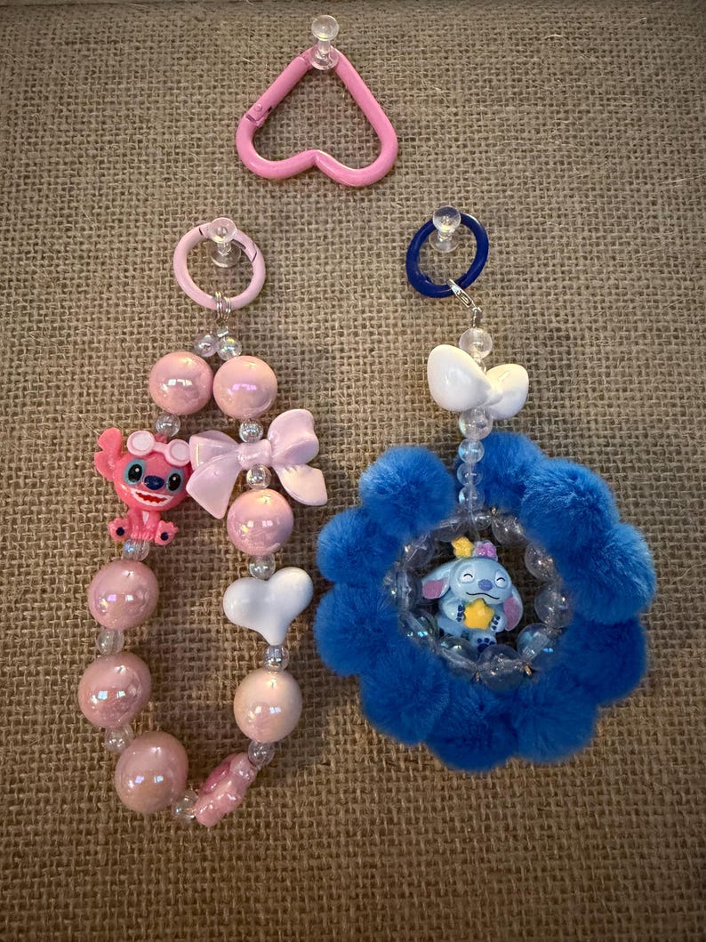 May include: Pink and blue beaded keychains with character charms. One keychain features a pink Stitch figure, pink beads, and a white bow. The other has a blue flower design with a Stitch figure inside. A pink heart-shaped carabiner is also visible.
