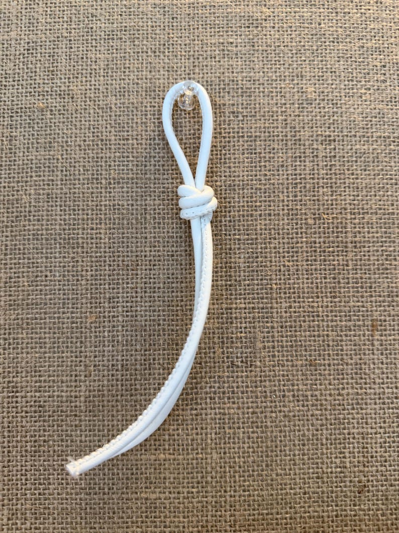May include: A white cord with a loop and knot, possibly for a drawstring or similar application. The cord is against a textured, tan background.