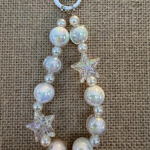 May include: A beaded keychain featuring iridescent, round beads and smaller pearl-like beads. Two clear, star-shaped charms are interspersed among the beads. The keychain has a white ring and suction cup for attachment.
