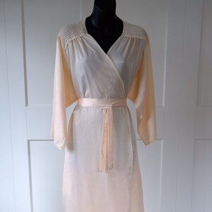 May include: A pale peach wrap robe with long sleeves and a matching tie belt. The robe has a textured neckline and a flowing, floor-length design. Ideal for loungewear or a vintage aesthetic. The robe's length is approximately 150 cm.