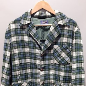 May include: A green, blue, and white checked jacket with a collared neckline, three brown buttons, and two front pockets. The jacket is hanging on a wooden hanger.