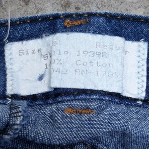 Puede incluir: Primer plano de unos vaqueros azules con una etiqueta blanca. La etiqueta dice "Size 5 Regular", "Style 1939R" y "100% Cotton". Los vaqueros tienen costuras visibles y un bot&oacute;n.