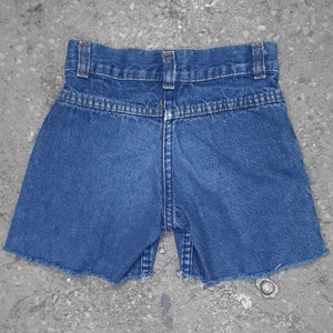 Puede incluir: Shorts vaqueros azules con dobladillo sin rematar. Los shorts tienen un dise&ntilde;o cl&aacute;sico de cinco bolsillos, trabillas para el cintur&oacute;n y cierre de bot&oacute;n y cremallera. Vista trasera que muestra la cintura y los detalles de costura.