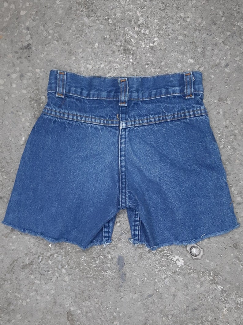 Puede incluir: Shorts vaqueros azules con dobladillo sin rematar. Los shorts tienen un dise&ntilde;o cl&aacute;sico de cinco bolsillos, trabillas para el cintur&oacute;n y cierre de bot&oacute;n y cremallera. Vista trasera que muestra la cintura y los detalles de costura.
