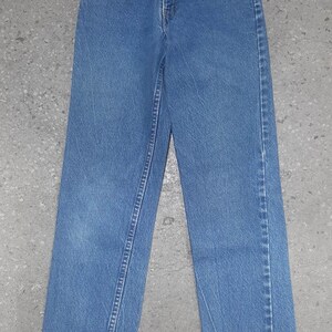 Puede incluir: Un par de vaqueros de mezclilla azul claro. Los vaqueros tienen un dise&ntilde;o cl&aacute;sico de cinco bolsillos, cierre de bot&oacute;n y cremallera, y corte recto. Los vaqueros est&aacute;n planos sobre una superficie gris.