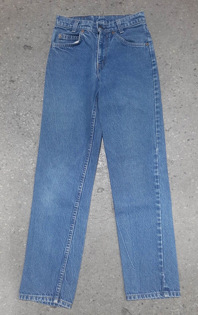 Puede incluir: Un par de vaqueros de mezclilla azul claro. Los vaqueros tienen un dise&ntilde;o cl&aacute;sico de cinco bolsillos, cierre de bot&oacute;n y cremallera, y corte recto. Los vaqueros est&aacute;n planos sobre una superficie gris.