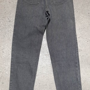 May include: Back view of a pair of charcoal gray denim jeans. The jeans have two back pockets and a small leather patch with red lettering. The jeans are a classic style, suitable for everyday wear.