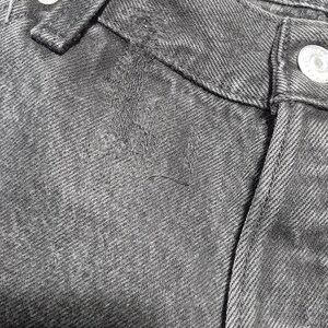 May include: Close-up of black denim jeans, showing the waistband, belt loop, and button closure. The fabric has a textured appearance with visible stitching and a worn look. The jeans are a classic style.