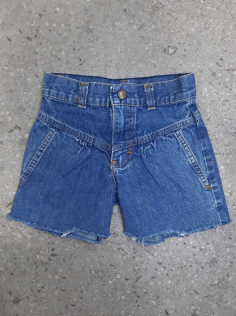 Puede incluir: Shorts vaqueros azules con cintura alta y un dise&ntilde;o de costura angular &uacute;nico. Los shorts tienen cierre de bot&oacute;n y bordes deshilachados en el dobladillo. Un estilo cl&aacute;sico e informal.
