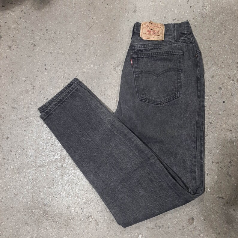 May include: Dark gray denim jeans with a classic five-pocket design. The jeans feature a red Levi's tag on the back pocket and a leather patch at the waistband. The jeans are a size 40.