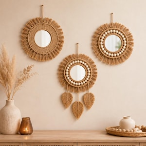 May include: Three circular wall mirrors featuring tan macrame cord frames with fringe. Two mirrors have simple cord borders, while the center mirror includes a ring of white wooden beads and three dangling macrame leaf-shaped accents below.