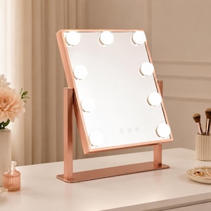 May include: A rectangular vanity mirror with a rose gold frame and a stand. The mirror features nine round LED light bulbs arranged around the perimeter and three touch-sensitive control buttons at the bottom center of the reflective glass surface.