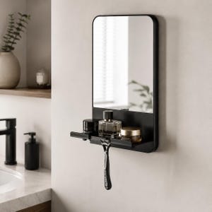 Puede incluir: Un espejo rectangular negro con esquinas redondeadas, con una estantería incorporada. La estantería contiene una botella de colonia, dos tarros y una maquinilla de afeitar. El espejo está montado en una pared blanca, creando una estética de baño moderno.