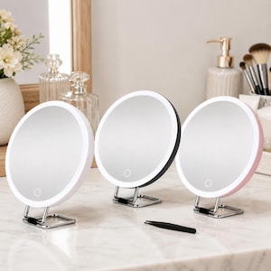 May include: Three circular vanity mirrors with integrated LED ring lights, each featuring a touch-sensitive power button on the glass surface. The mirrors are supported by silver-toned metal stands and come in white, black, and light pink frames.