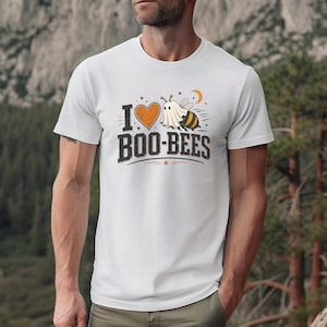 May include: White t-shirt with a Halloween-themed graphic. The design features the text "I Boo-Bees" with a heart, a ghost, a bee, and a crescent moon. The shirt is a short-sleeved crew neck.