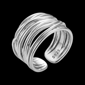 May include: A wide silver ring featuring a multi-strand design with several overlapping, polished wire-like bands that create a layered appearance. The ring has an open-back construction and is clearly stamped with the text S925 on the inner band.