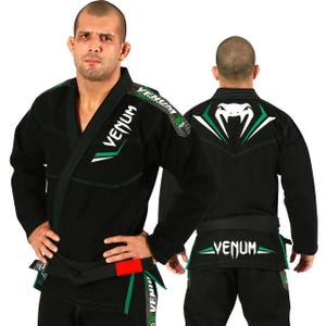 Può includere: Un gi da Jiu-Jitsu brasiliano nero con il logo Venum in bianco e verde. La giacca mostra il nome del marchio sul petto e sulla spalla, mentre la schiena presenta una grande grafica a testa di serpente. È indossata una cintura nera con una linguetta rossa.