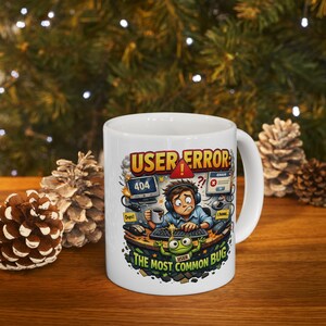 May include: White ceramic mug with a humorous illustration. The design features a distressed person at a computer with error messages, the text "USER ERROR" and "THE MOST COMMON BUG".