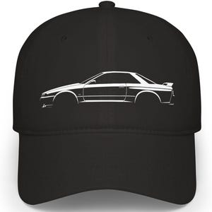 May include: Black baseball cap featuring a white outline of a sports car. The car design is on the front of the cap. The cap has a curved brim and a button on top.