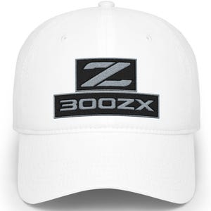 May include: White baseball cap featuring a black and gray embroidered logo with the letter "Z" above the text "300ZX". The cap has a curved brim and a structured crown. A classic accessory for car enthusiasts.