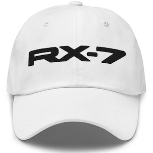 May include: A white baseball cap with the black text "RX-7" across the front. The hat has a curved brim and a button on top. The hat is made of a soft material.