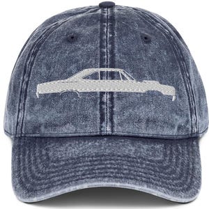 May include: A denim blue baseball cap with a faded, vintage look. The cap features a white embroidered outline of a classic car on the front. The cap has a curved brim and an adjustable strap at the back for a comfortable fit.