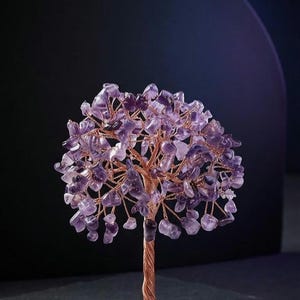 May include: A decorative tree sculpture featuring a trunk and branches made of twisted copper wire. The leaves consist of numerous small, polished purple amethyst stone chips. The tree is mounted on a circular base inlaid with various stone fragments.