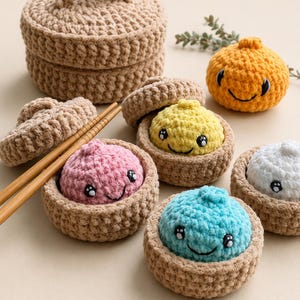 May include: A collection of crocheted items including a large tan lidded basket, four small tan lidded baskets containing round plush figures in pink, yellow, blue, and white, an orange plush figure, and a pair of wooden chopsticks.