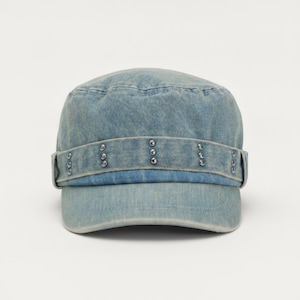 Può includere: Un berretto in stile militare in denim azzurro con corona strutturata e parte superiore piatta. Una fascia orizzontale avvolge la base, decorata con piccoli rivetti metallici color argento distanziati uniformemente. Il tessuto ha una consistenza sbiadita.