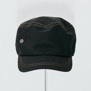 May include: A black military-style cadet cap featuring a flat top and a short, curved brim. The hat is constructed from a solid black fabric with contrasting brown stitching along the seams and brim, and includes a small circular metal emblem.