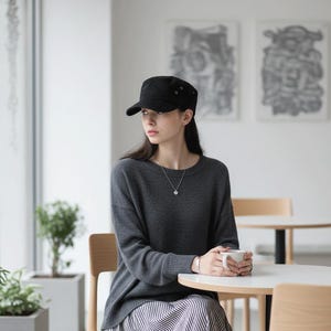 May include: A black military-style cap with a flat top and side button details, paired with a dark gray long-sleeved sweater and a black and white striped skirt. The ensemble includes a simple silver chain necklace and a thin silver wrist cuff.