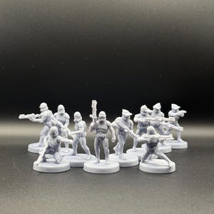 May include: A collection of gray miniature figurines of soldiers in combat poses, each holding a weapon. The figures are standing on circular bases. The background is a solid dark gray.