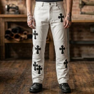 May include: Off-white leather pants featuring a five-pocket design, a button fly, and black cross-shaped patches stitched onto the front of the legs. The pants are paired with black leather boots, showcasing a structured fit and visible seams.