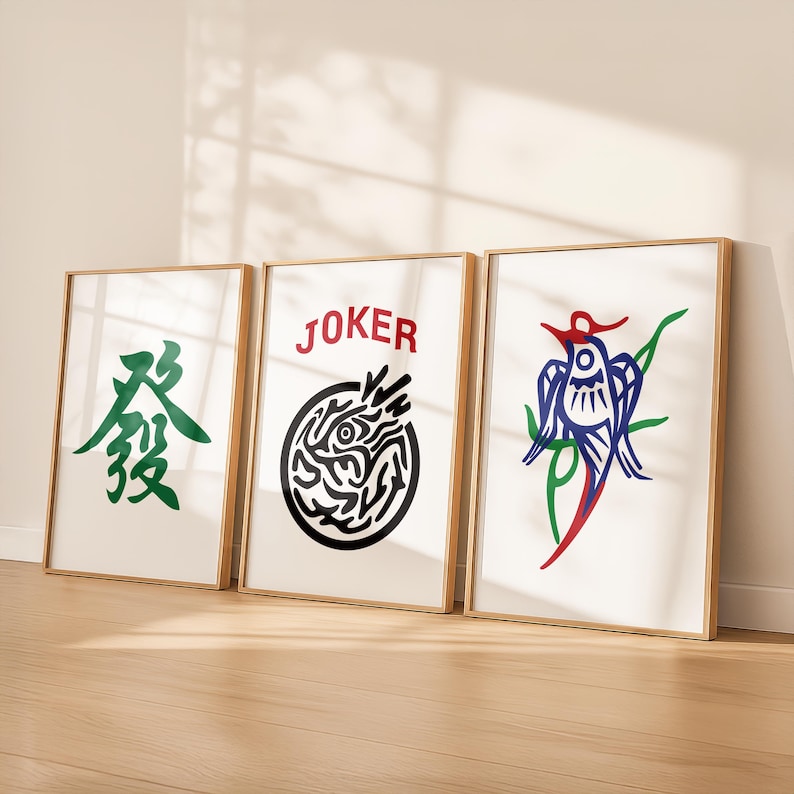May include: Three framed art prints with gold-colored frames. The prints feature graphic designs: a green Chinese character, a black and white circular design with the word "JOKER" in red, and a blue, red, and green bird design.