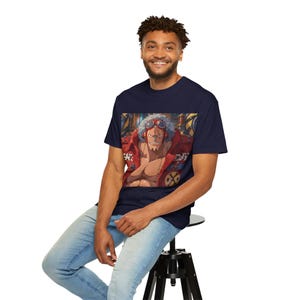 May include: A navy blue short-sleeve t-shirt featuring a graphic print of a cartoon character with spiky white hair, red goggles, and a red jacket. The character is depicted from the chest up against a mechanical background with industrial details.