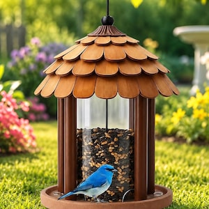 May include: A wooden bird feeder with a shingle-style roof and a clear cylindrical seed container. A small blue bird perches on the feeder's base, surrounded by green grass and flowers. The feeder is filled with seeds.