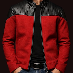 Può includere: Giacca rossa con colletto e pannelli sulle spalle in pelle nera. La giacca ha una cerniera a tutta lunghezza e due tasche anteriori. La persona indossa una maglietta nera e jeans blu.