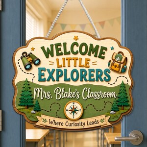 May include: A decorative wooden sign hanging by a white rope, featuring the text "WELCOME LITTLE EXPLORERS" and "Mrs. Blake's Classroom" with "Where Curiosity Leads" below. The design includes illustrations of binoculars, a backpack, trees, and a compass.
