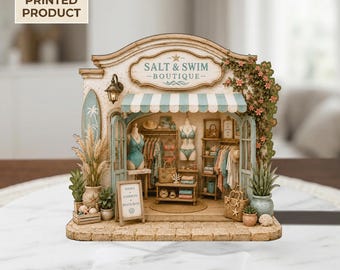 May include: A 2D flat printed miniature boutique shop titled Salt & Swim Boutique. The shop features a teal and white striped awning, a surfboard, mannequins displaying swimwear, clothing racks, shelves with accessories, and potted plants.