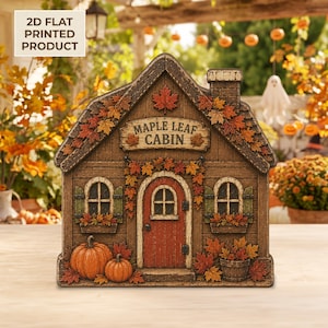 May include: A 2D flat printed product shaped like a cabin with the text Maple Leaf Cabin. The design features a brown wooden structure with a red door, green shutters, orange pumpkins, and autumn maple leaves in shades of red, orange, and yellow.