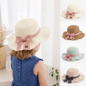 Può includere: Un cappello da sole in paglia con tesa ondulata e un fiocco in tessuto. Il cappello è disponibile in crema, marrone chiaro, verde chiaro e rosa chiaro. Ogni cappello presenta un nastro abbinato o a contrasto annodato alla base della calotta.