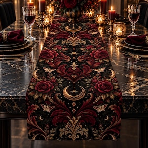 May include: A black table runner featuring a repeating pattern of deep red roses, golden crescent moons, stars, and moths. The intricate design includes ornate scrolling foliage in shades of red and gold, creating a symmetrical, detailed textile piece.