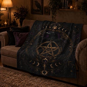 May include: A dark-colored throw blanket featuring a central gold pentagram design surrounded by a circular lunar phase motif and a raven illustration. The blanket displays intricate filigree patterns, stars, and celestial elements in gold and purple.